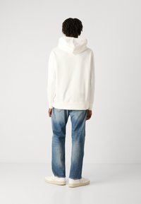 Sudadera blanca con capucha, combinada con unos vaqueros rectos azules y zapatillas blancas, con una textura suave y puños acanalados.