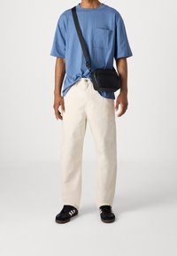 Camiseta de algodón azul con un bolsillo en el pecho, pantalones vaqueros de pierna ancha color crema y zapatillas negras con rayas blancas. Bolso bandolera de cuero negro.