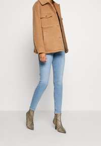 Chaqueta de mezcla de lana marrón con dos bolsillos en el pecho, combinada con jeans skinny de color azul claro y botines de tacón con estampado de serpiente texturizado.