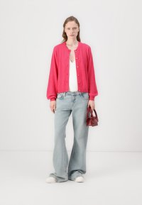 Rosa ribbad cardigan med guldknappar, vit topp, ljusblå utsvängda jeans och en liten röd handväska. Skorna inkluderar vita sneakers.