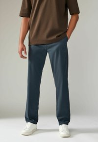 Camiseta marrón de manga corta combinada con pantalones anchos de color azul oscuro y zapatillas blancas. La tela parece suave, con un diseño sencillo.