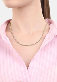 Collana a catena intrecciata in oro e argento, indossata al collo di una donna sopra una camicia a righe rosa con colletto.