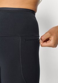 Les leggings noirs taille haute présentent une texture lisse, une poche zippée sur le côté et des coutures contrastantes le long des seams pour plus de détails.
