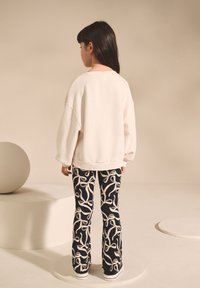 White sweatshirt with drop shoulders paired with black pants featuring white ribbon patterns. Texture appears soft and casual.