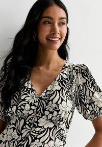 Vestido de estampado floral con un diseño en blanco y negro, escote en V, mangas cortas abullonadas y un cuerpo ajustado. Tejido texturizado con botones.