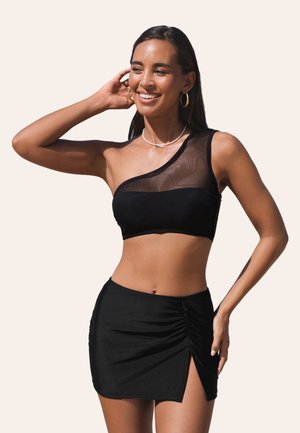 Černý bikiny top s designem na jedno rameno, doplněný síťovinou. Doplněno odpovídající černou sukní se shrnutím a bočním rozparkem.