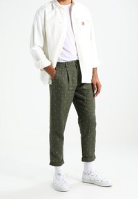 Lehce bílá košile přes jednoduché bílé tričko, doplněná olivově zelenými kalhotami s bílými puntíky a vyhrnutými lemy. Bílé tenisky.