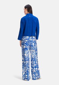 Cropped blue linen jacket with a collar, paired with wide-leg pants featuring a white fabric adorned with blue abstract patterns.