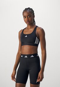 Svart trenings-BH og høytlivsshorts med hvit tre-stripes design. Jevn tekstur og tettsittende fasong for aktiv bruk.