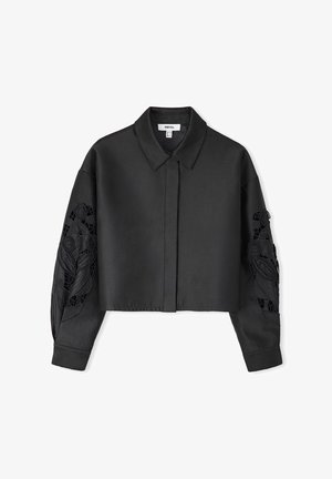 Black cropped shirt with a classic collar, satin finish, and intricate floral lace detailing on sleeves. Button-up front and long sleeves.