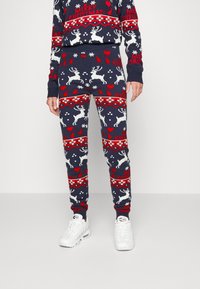 Stickad pyjamasuppsättning med mörkblå bakgrund, röda och vita renar, hjärtan och snöflingor. Tröjan har ribbade ärmslut och midja.