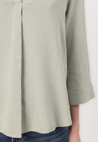 Ljusgrön, löst sittande blus med trekvartslånga ärmar, textil med struktur, subtil plissé fram och uppvikta ärmslut.