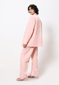 Rosafarbener oversized Blazer mit lockerer Passform und hinterem Schlitzausschnitt, kombiniert mit weit geschnittenen Hosen und hohen Sandalen, die ein minimalistisches Design aufweisen.