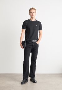 Sort kortærmet t-shirt med hvid kant, parret med sorte jeans og et bælte. Tilbehør inkluderer en lille sort pung. Glat stof, tætsiddende design.