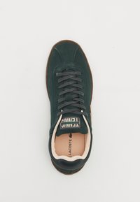 Zöld velúr sneaker szürke fűzőkkel, kerek orral és bézs béléssel. Texturált gumitalp jellemzi, valamint egy "Tennis" felirat a külső oldalán.