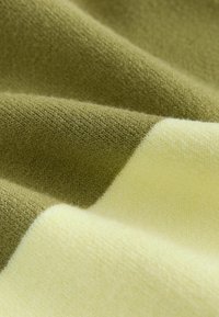 Strickstoff mit abwechselnden Abschnitten in Grün und blassem Gelb, der eine weiche Textur und ein glattes Finish zeigt. Das detaillierte Webmuster ist sichtbar.