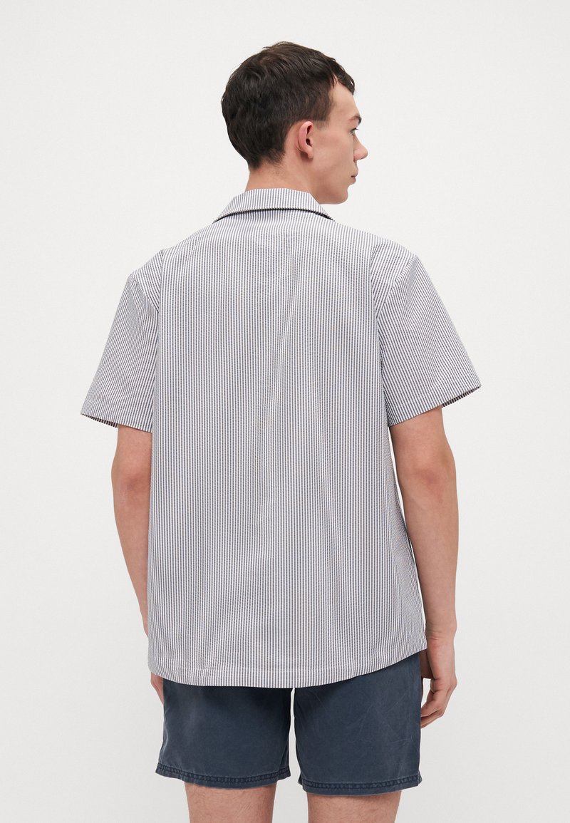 Chemise à manches courtes, col, en tissu rayé blanc et bleu marine. Présente une coupe décontractée et un ourlet droit à l'arrière.