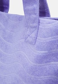 Sac fourre-tout en tissu violet avec un motif ondulé texturé, une texture douce et des poignées solides. Le matériau semble absorbant et moelleux.
