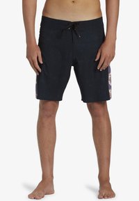 Bañador negro con acentos florales en púrpura y crema en los laterales. Cuenta con una cintura ajustable y un acabado texturizado.
