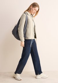 Giacca in pile grigio chiaro, jeans a gamba larga blu scuro e sneakers bianche. La giacca ha un bottone anteriore e una vestibilità rilassata.