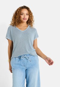 Top de punto texturizado en azul claro con escote en V, combinado con pantalones de mezclilla claros con cordón. Mangas cortas y ajuste relajado.