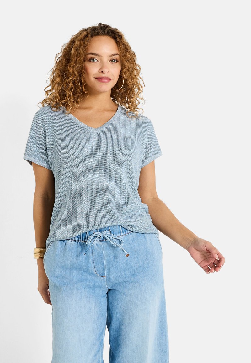 Top de punto texturizado en azul claro con escote en V, combinado con pantalones de mezclilla claros con cordón. Mangas cortas y ajuste relajado.