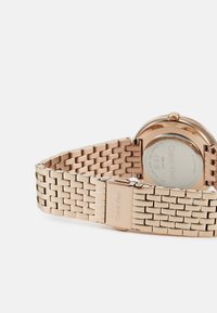 Reloj de metal en color oro rosa con un diseño de pulsera trenzada, que presenta un acabado suave y un cierre de marca. La parte trasera revela una caja circular minimalista.