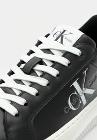 Czarne skórzane sneakersy z białymi sznurówkami, z wyraźnym logo "CK" oraz napisem "Calvin Klein Jeans" na języku i boku.