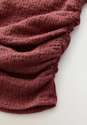 Texturovaná, tmavě burgundská látka se skládá v jemných záhybech, má pletený vzor s mírně vyvýšeným povrchem a jemným žebrováním.