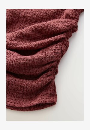 Textured, dark burgundy fabric drapes in soft folds, featuring a knit pattern with a slightly raised surface and subtle ribbing.