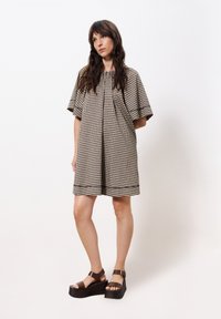 Braun- und cremefarbendes karierter Kleid mit kurzen Ärmeln, rundem Ausschnitt und Raffung. Kombiniert mit braunen klobigen Plateausandalen.