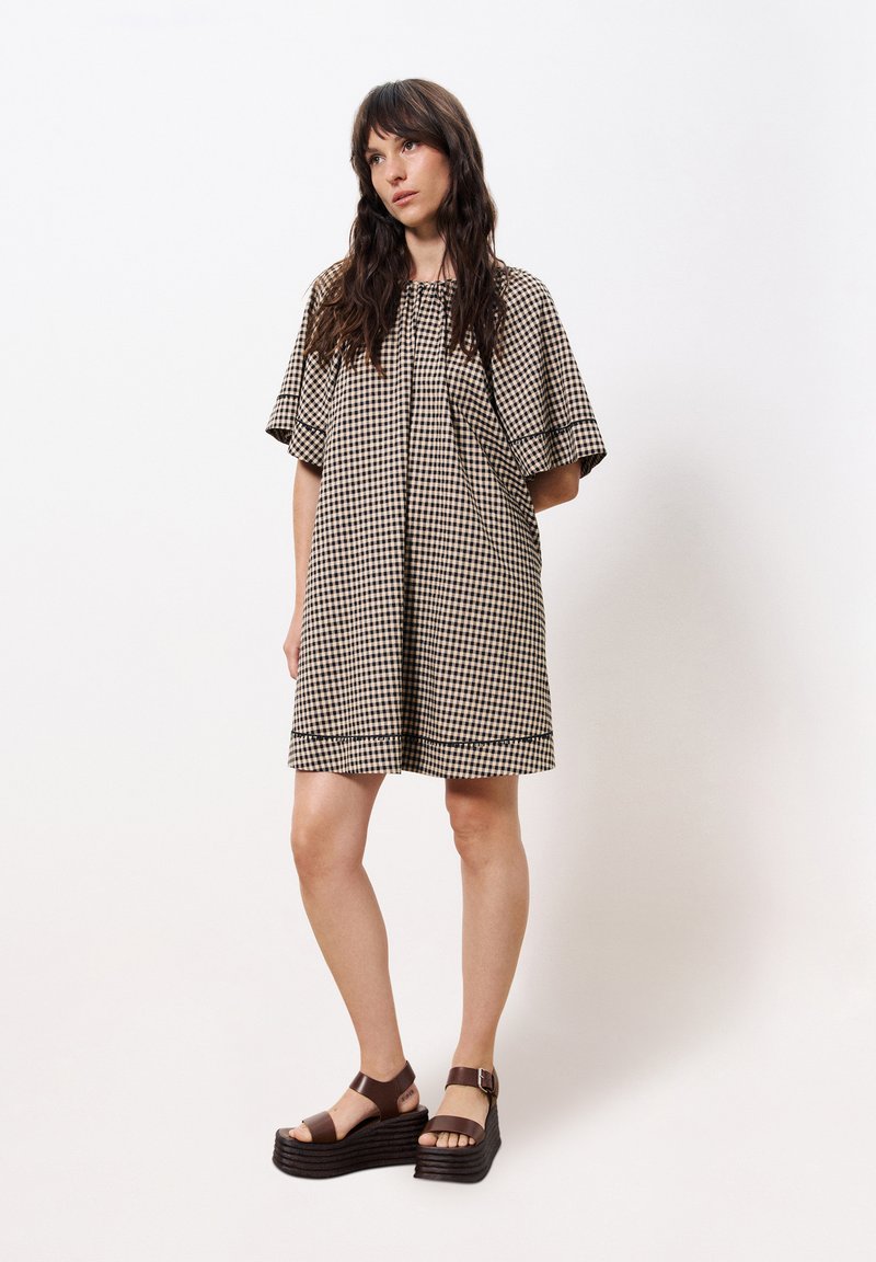 Braun- und cremefarbendes karierter Kleid mit kurzen Ärmeln, rundem Ausschnitt und Raffung. Kombiniert mit braunen klobigen Plateausandalen.