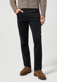 Zwarte corduroy broeken met een rechte pasvorm, voorzien van zijzakken en een zachte textuur, gedragen met bruine suède schoenen.