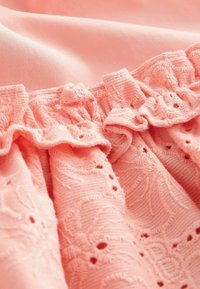 Tissu rose présentant un bord froncé avec des motifs floraux brodés et de petites découpes, mettant en valeur des détails de surface texturés.