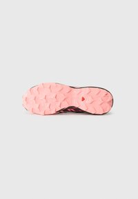 Semelle en caoutchouc rose avec un motif de semelle agressif et multidirectionnel ; la tige présente des accents noirs et des surfaces texturées, conçues pour l'adhérence.