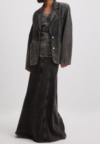 Blazer in denim nero con cuciture a contrasto, abbinato a un top aderente e una lunga gonna, caratterizzati da una texture liscia e dettagli con bottoni.