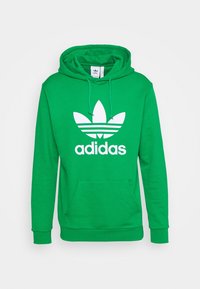 Zelená bavlněná mikina s kapucí, předními kapsami kangaroo, stahovací šňůrkou na kapuci a velkým bílým logem Adidas trefoil na hrudi.
