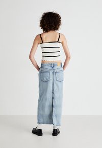 White and black striped crop top with thin straps, paired with a light blue, long denim skirt featuring back pockets and a slight fray at the hem.