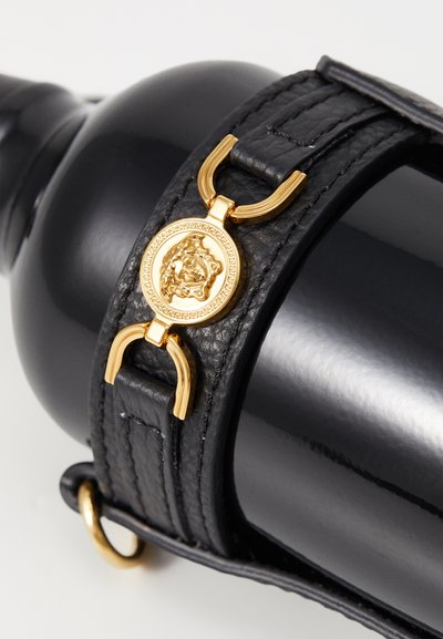 Sangle en cuir noir avec quincaillerie en or, présentant un médaillon circulaire avec un design de tête de lion et des détails texturés. Surface lisse et brillante.