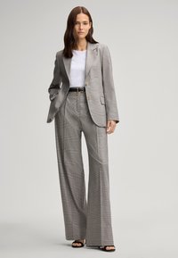 Grijs gestreept pak met gestructureerde blazer en wijde broekspijpen, met een wit T-shirt, zwarte riem en open-teen zwarte hakken.