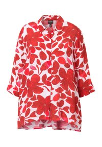 Chemise blanche boutonnée avec un motif floral rouge, manches trois-quarts et un ourlet arrière légèrement plus long.