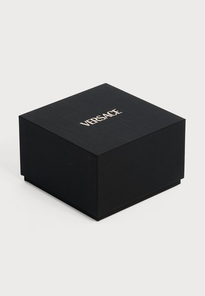 Boîte carrée noire Versace avec surface texturée et logo blanc Versace centré sur le couvercle, sur un fond clair uni.