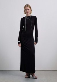 Vestido negro de manga larga con silueta ajustada, que presenta un escote redondo, detalles fruncidos y detalles plateados contrastantes en los puños.