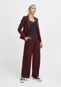 Burgunderfarbener Blazer und passende weite Hose mit einem schwarzen Spitzen-Camisole. Das Outfit zeichnet sich durch einen maßgeschneiderten Schnitt und eine glatte Stofftextur aus.