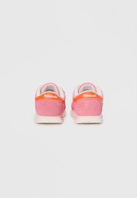 Roze suede tenisice s bijelim potplatima, s narančastim naglaskom i Reebok logotipom na peti. Mekana tekstura i zaobljen oblik.