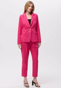 Fuksija odijelo koje se sastoji od uskog sakoa s reverima i hlača prilagođenog kroja. Glatka tkanina, uparen s crnim sandalama na visoku petu.