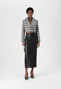Svart faux lær maxi skjørt og cropped tweed jakke med et grått og hvitt rutemønster. Modellen holder en liten hvit håndveske.