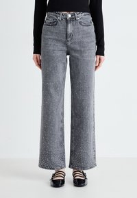 Jeans de tiro alto y pierna ancha hechos de mezclilla gris, con adornos de tachuelas en la parte inferior de las piernas y diseño clásico de cinco bolsillos.