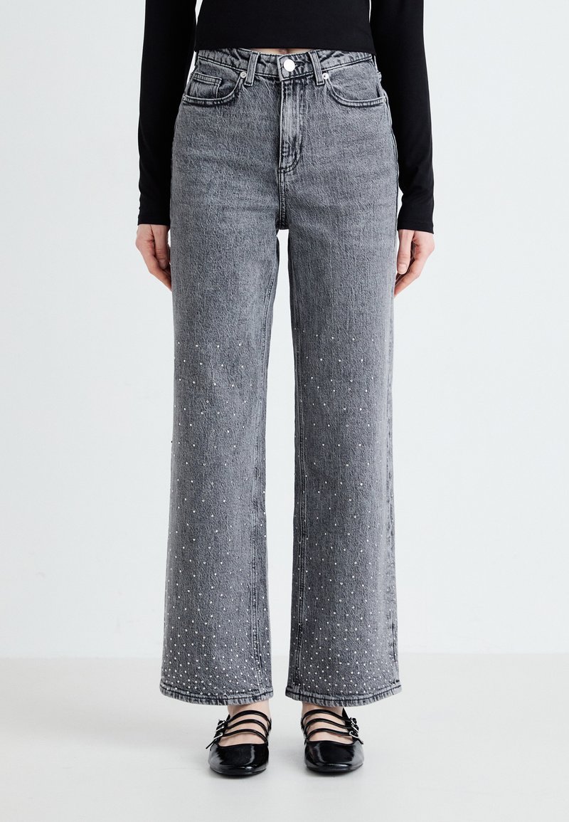 Jeans de tiro alto y pierna ancha hechos de mezclilla gris, con adornos de tachuelas en la parte inferior de las piernas y diseño clásico de cinco bolsillos.