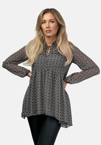 Czarna bluzka z białymi kwiatowymi wzorami, marszczonym dekoltem i długimi rękawami. Swobodny krój, lekko dłuższa z tyłu niż z przodu.